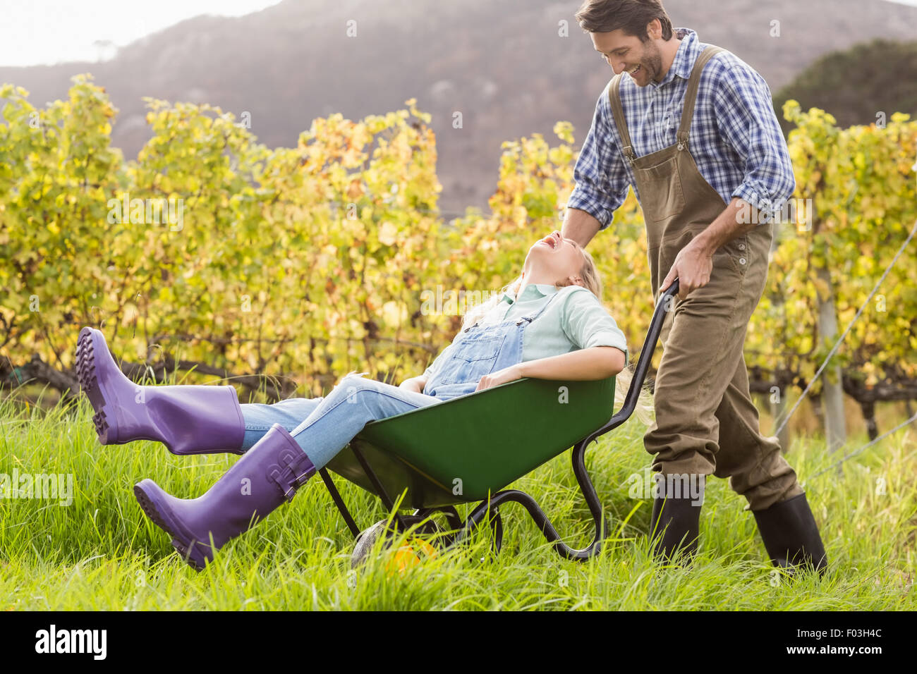 Laughing couple in dungarees pushing a wheelbarrow Stock Photo