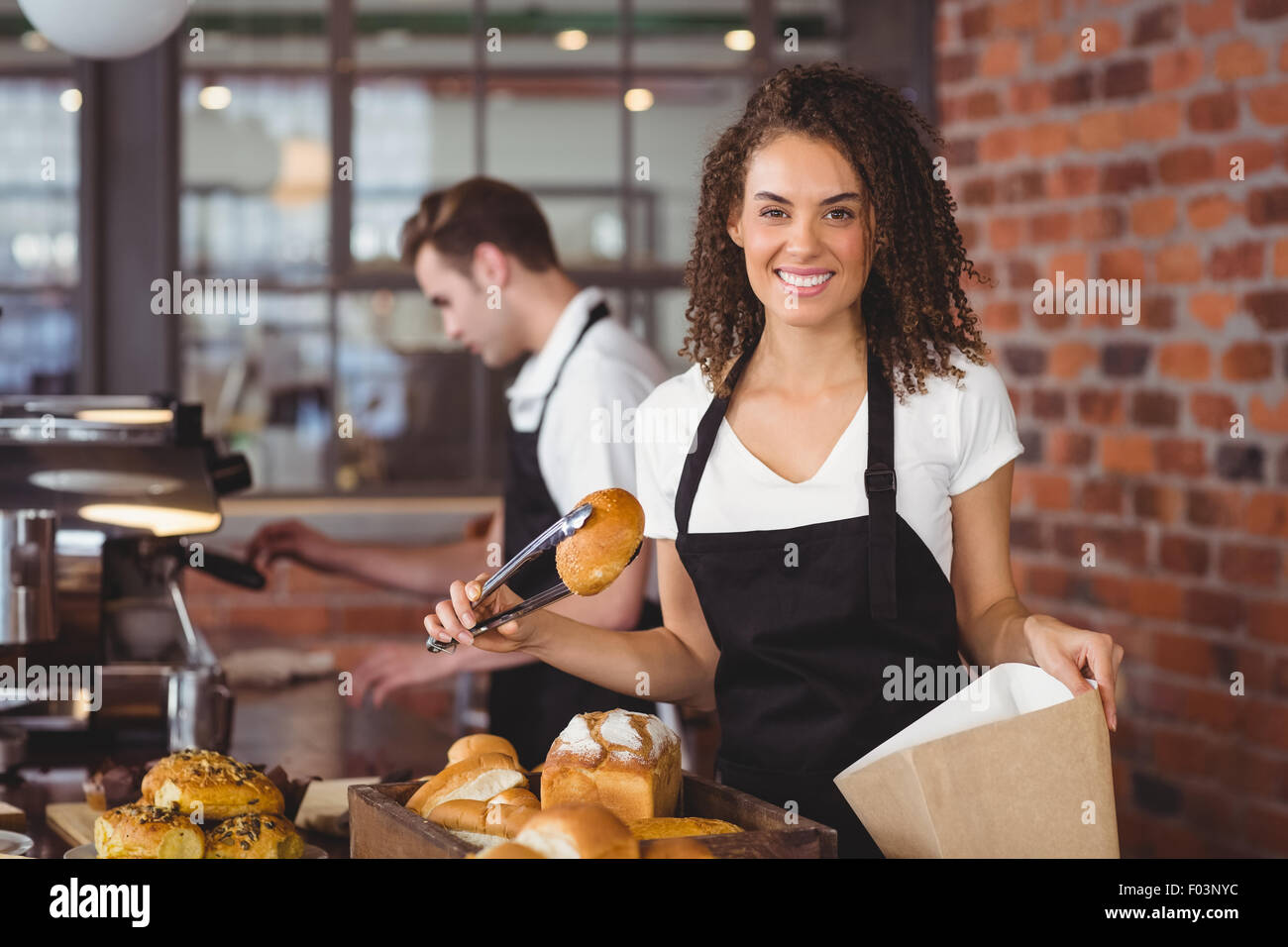 Smiling waitress putting bread roll in paper bag Stock Photo
