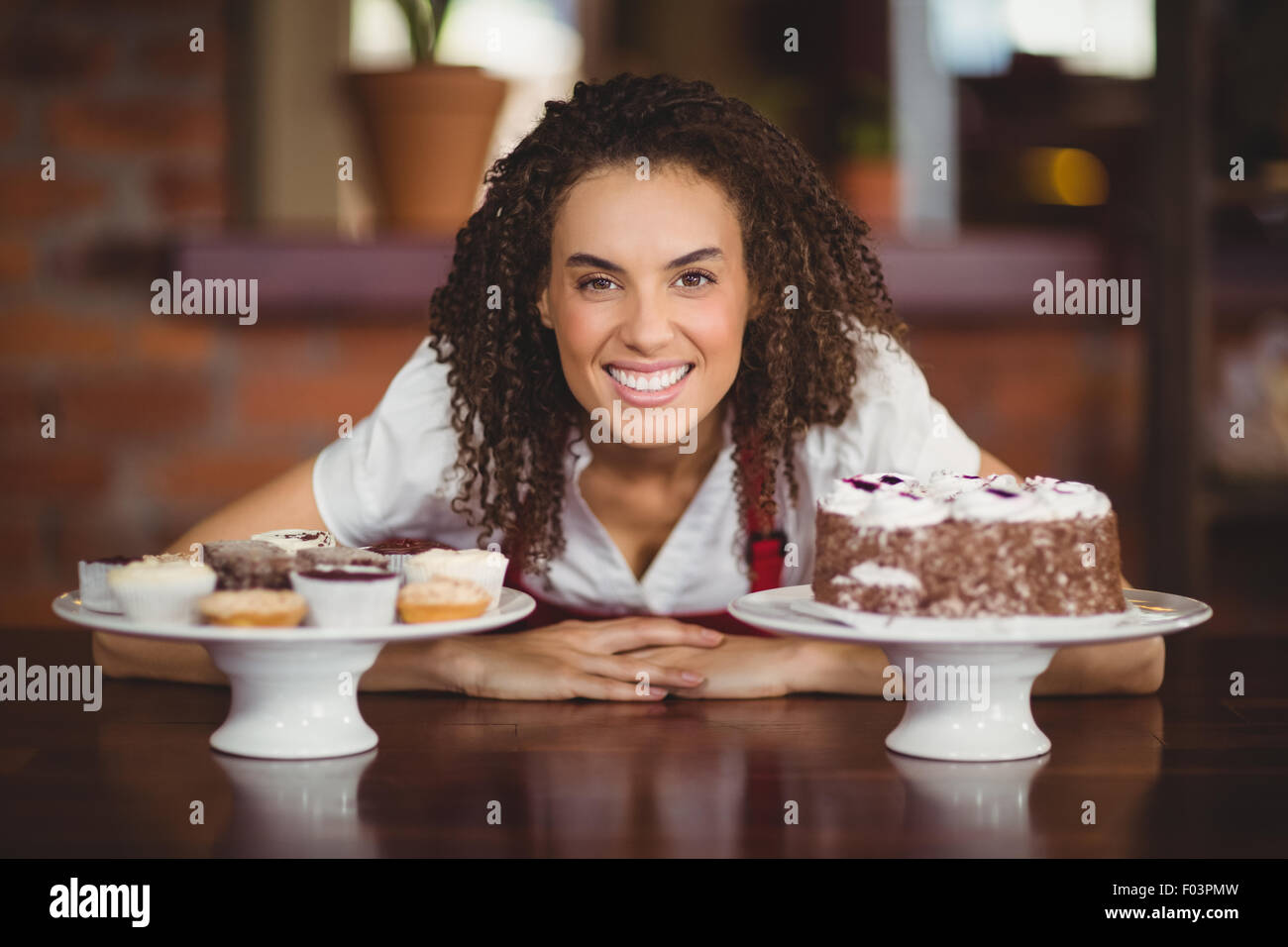 Waitress bending over chocolate cake and cupcakes Stock Photo