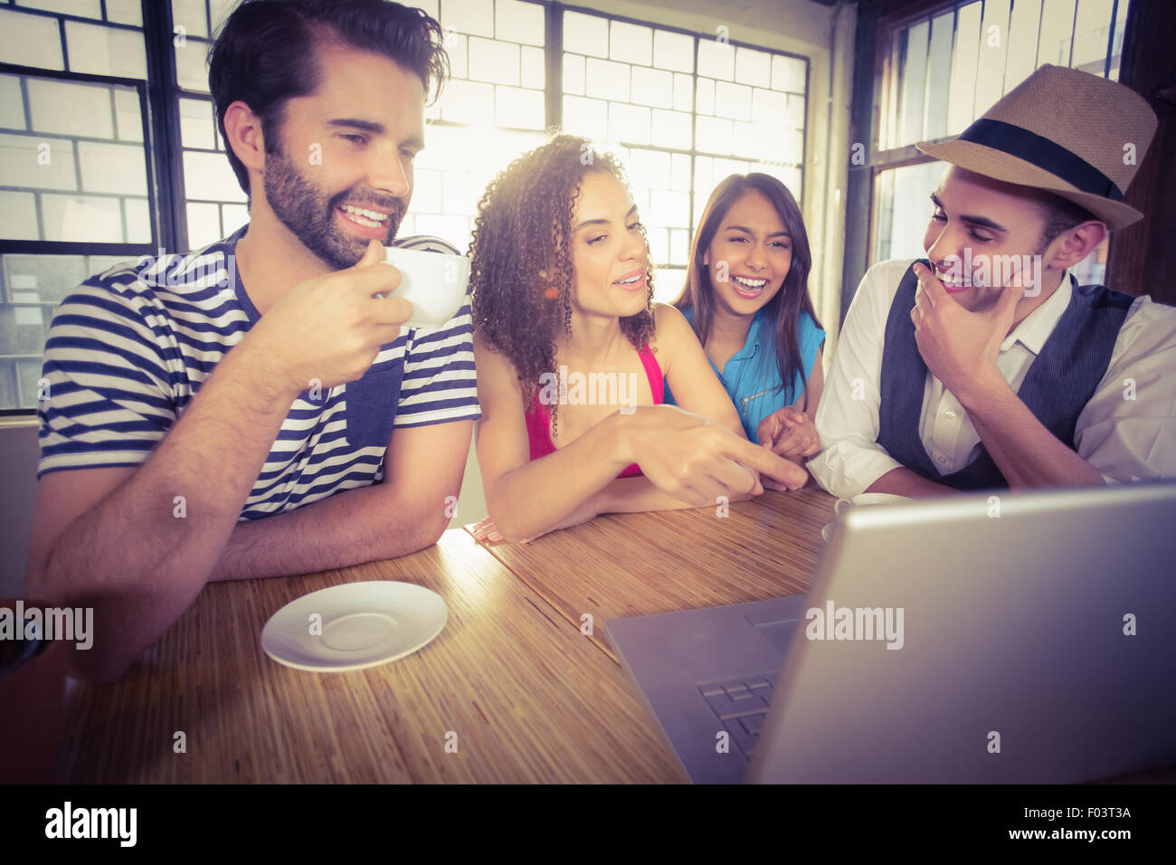 Laughing friends drinking coffee and looking at laptop Stock Photo