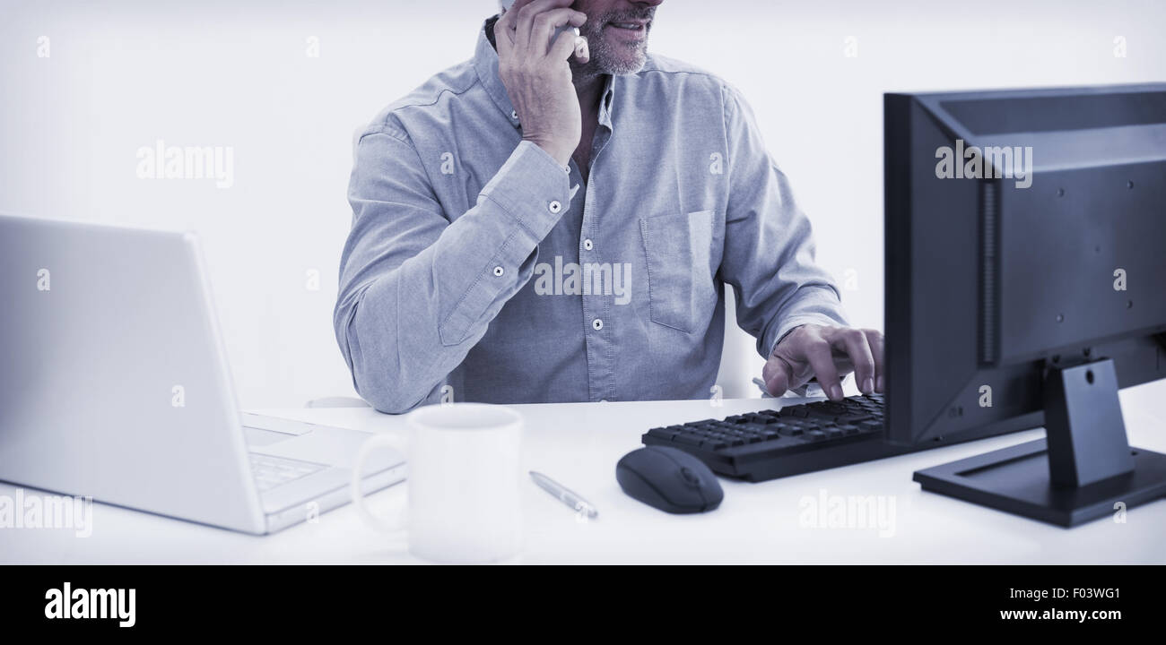 Businessman with cellphone, laptop and computer at desk Stock Photo