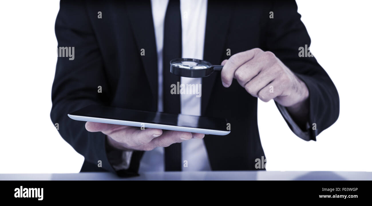 Businessman looking at his tablet through magnifying glass Stock Photo