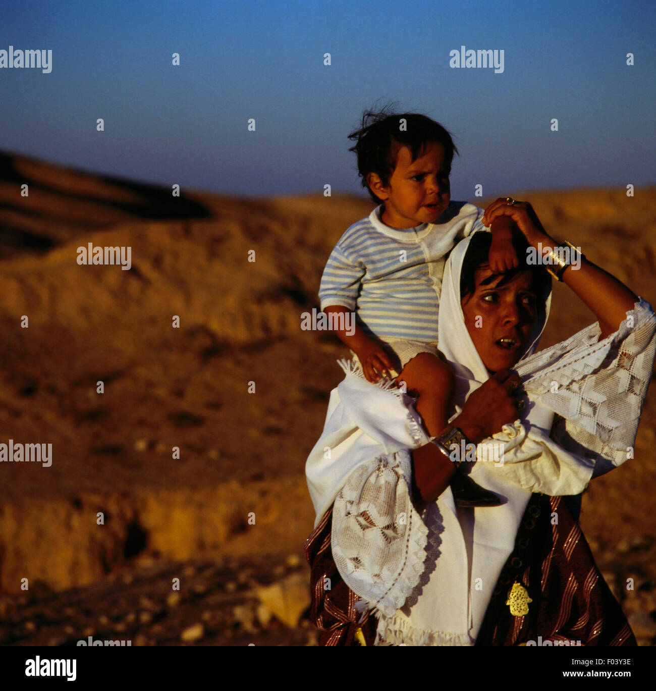 Woman in traditional clothes with a child on her shoulders, Matmata, Tunisia. Stock Photo