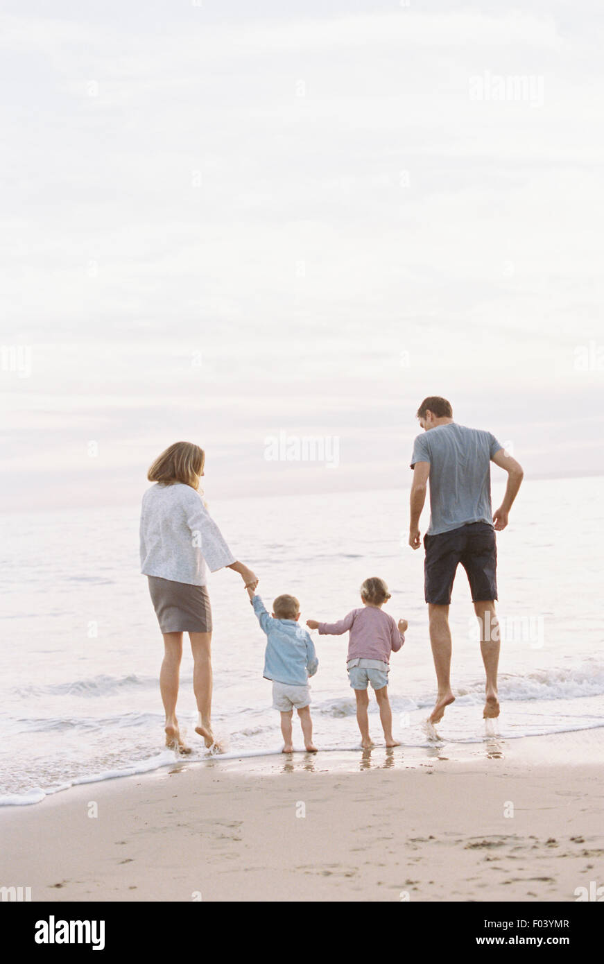 Couple playing with their son and daughter on a sandy beach by the ocean, holding hands. Stock Photo