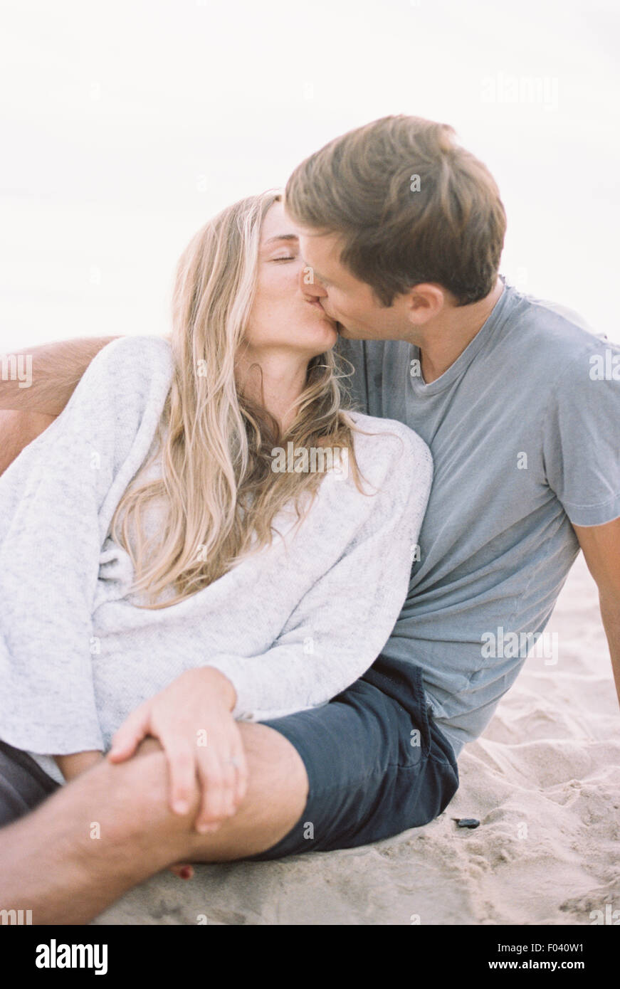 A couple sitting close on a beach, a man and woman with their arms around each other and heads together. Stock Photo