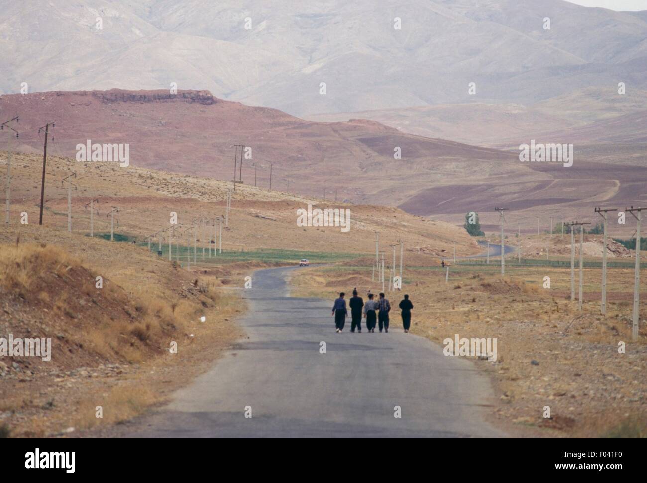 Men walking down a road in an arid landscape, Iranian Azerbaijan, Iran. Stock Photo