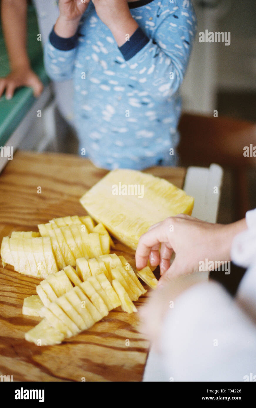 Woman cutting a fresh pineapple for her children. Stock Photo