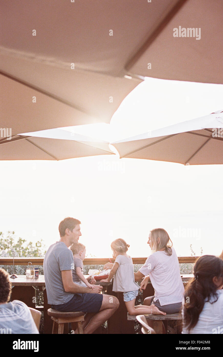 Couple sitting under a parasol in a restaurant with their son and daughter. Stock Photo