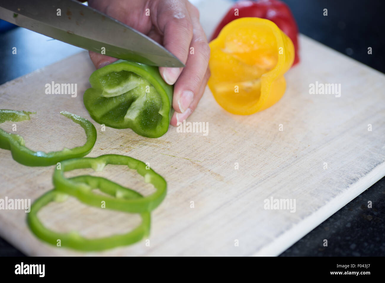 A  Man preparing a green, yellow and red pepper for a meal Stock Photo