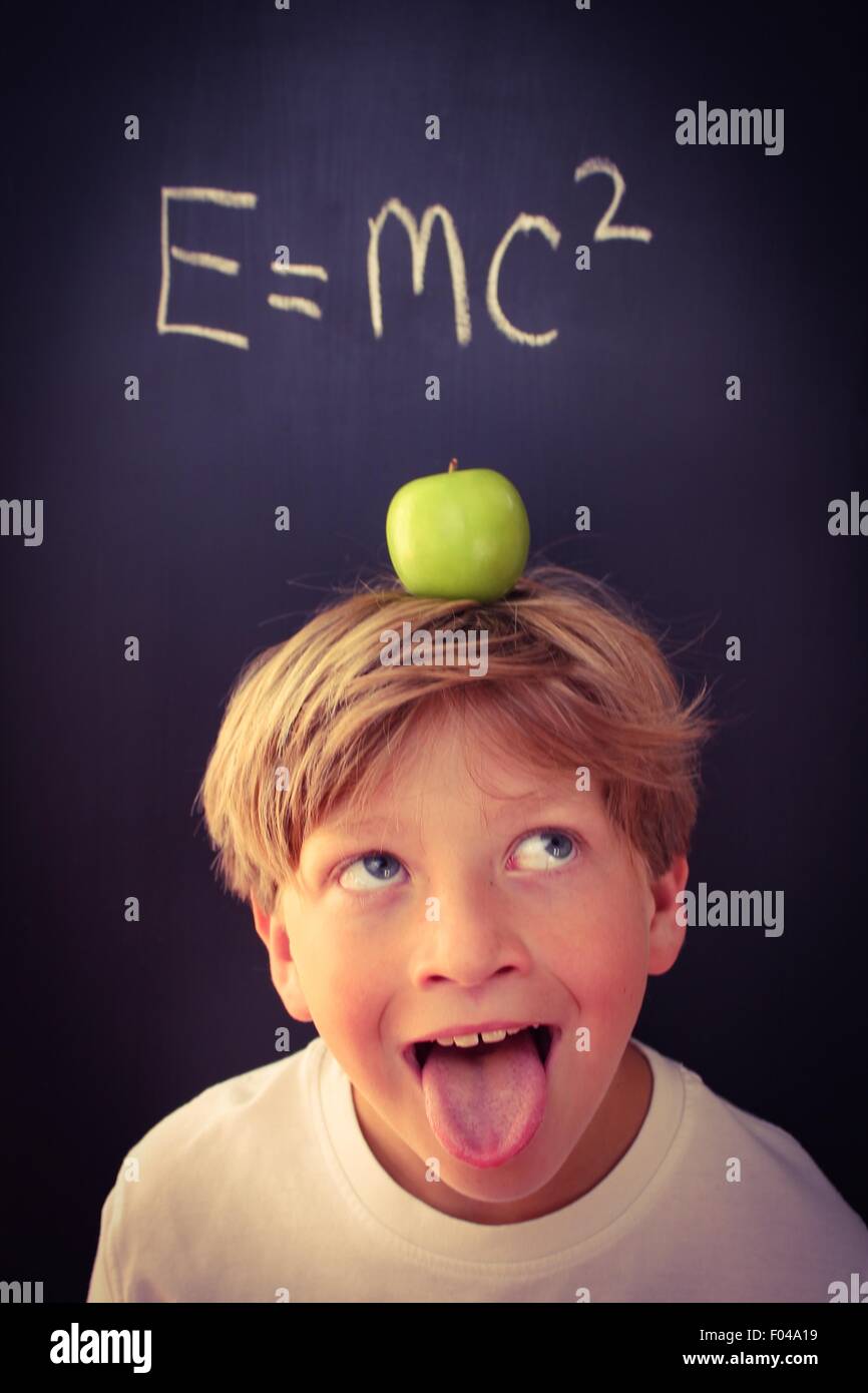 Child with his tongue hanging out looking at a physics equation with an apple on his head Stock Photo