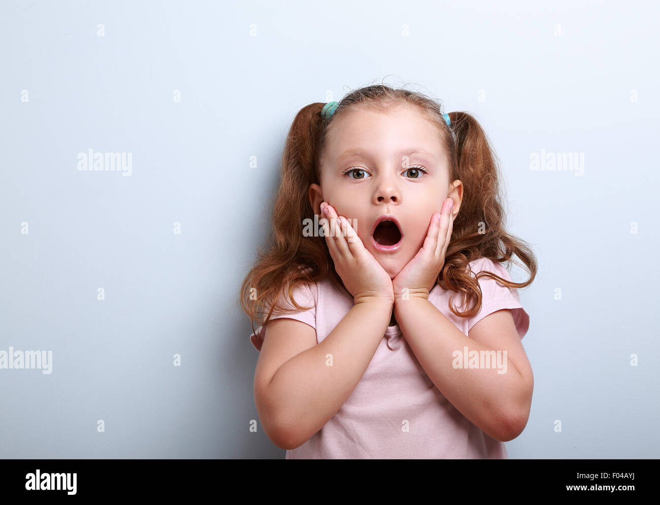Fun surprising kid girl with opened mouth looking on blue background with empty copy space Stock Photo