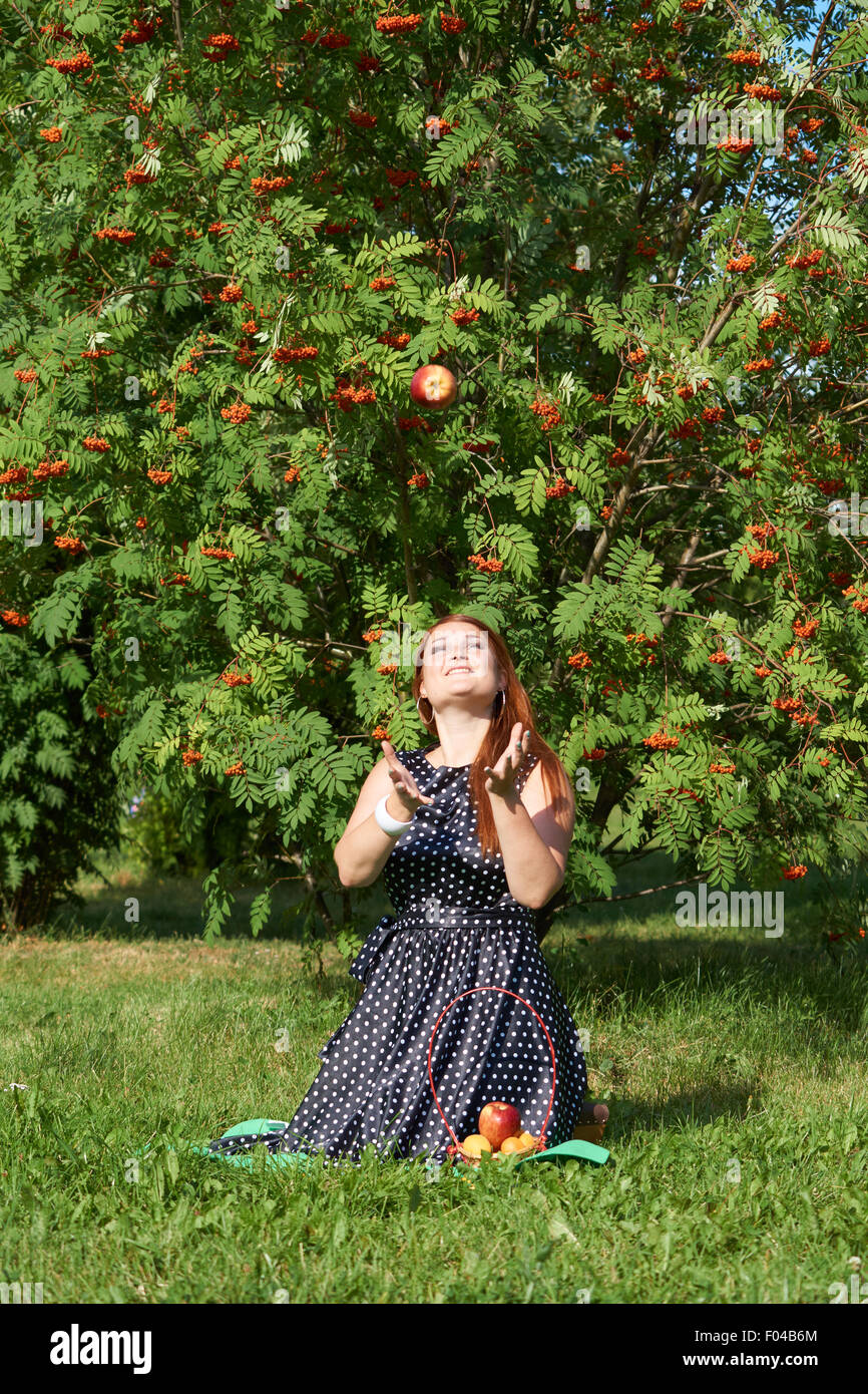 Red girl throws up apple on the meadow of the park Stock Photo