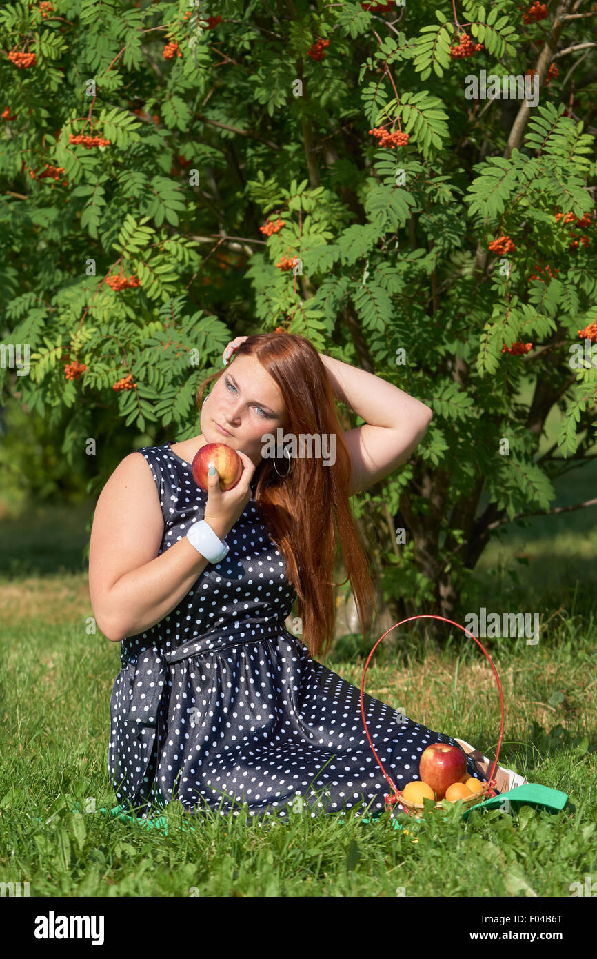 Red girl holds apple in her hand at picnic Stock Photo