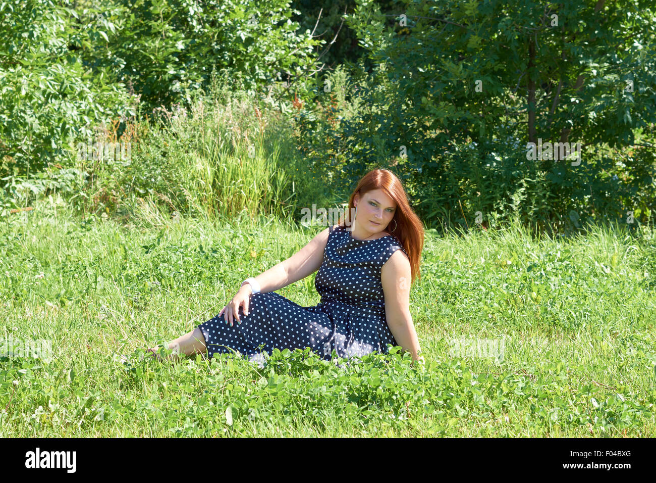 One girl with red hair sits in the meadow in the park Stock Photo