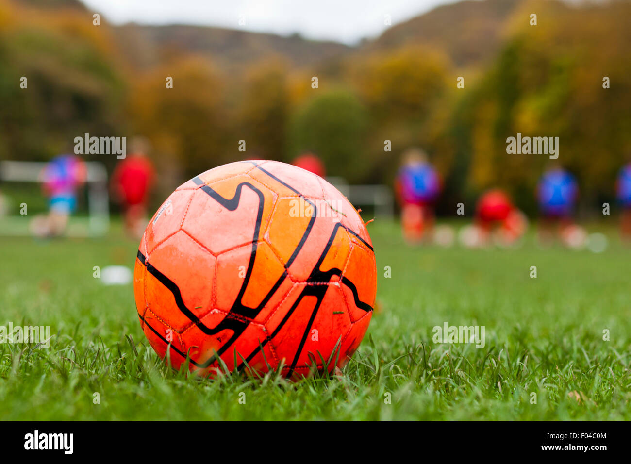 Football with anonymous young footballers in the distance, England Stock Photo