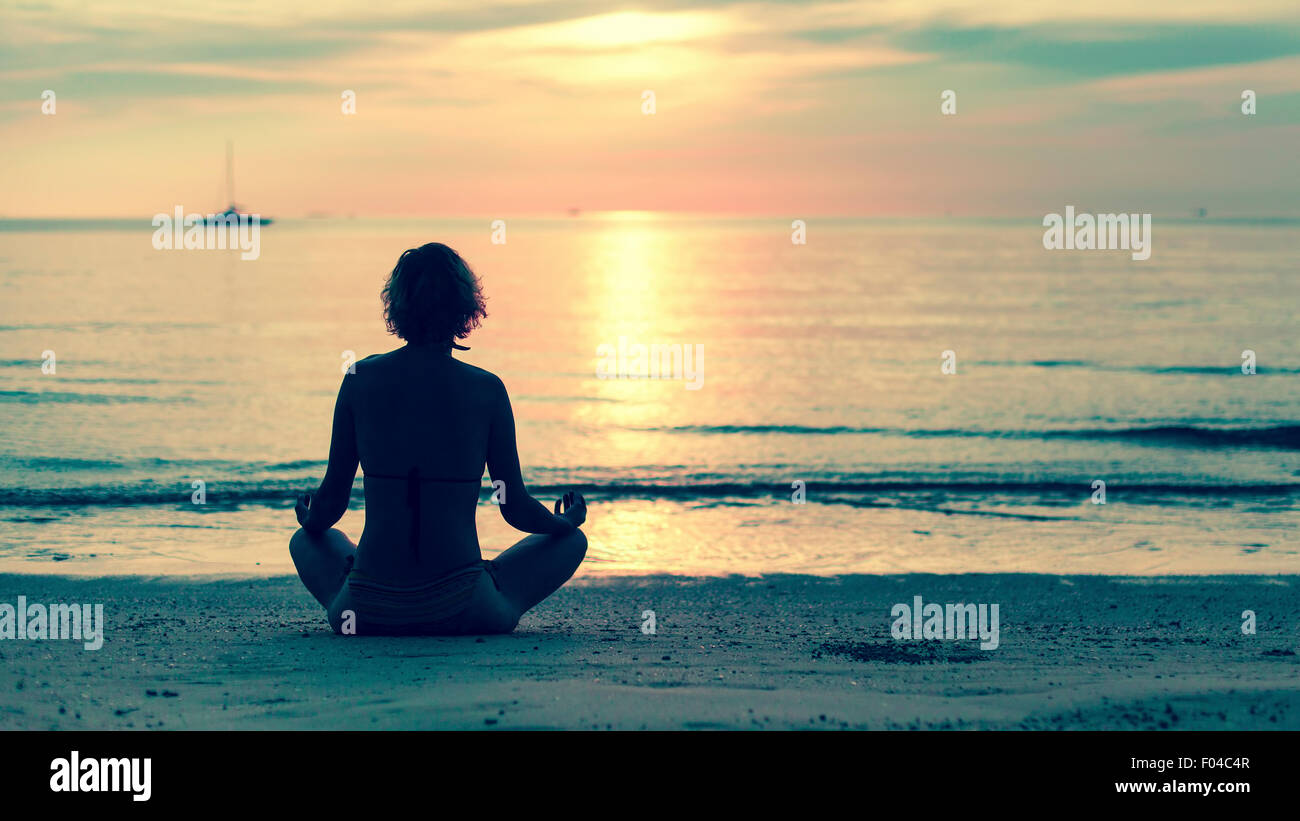 Yoga woman sitting in lotus pose on the beach during amazing sunset ...
