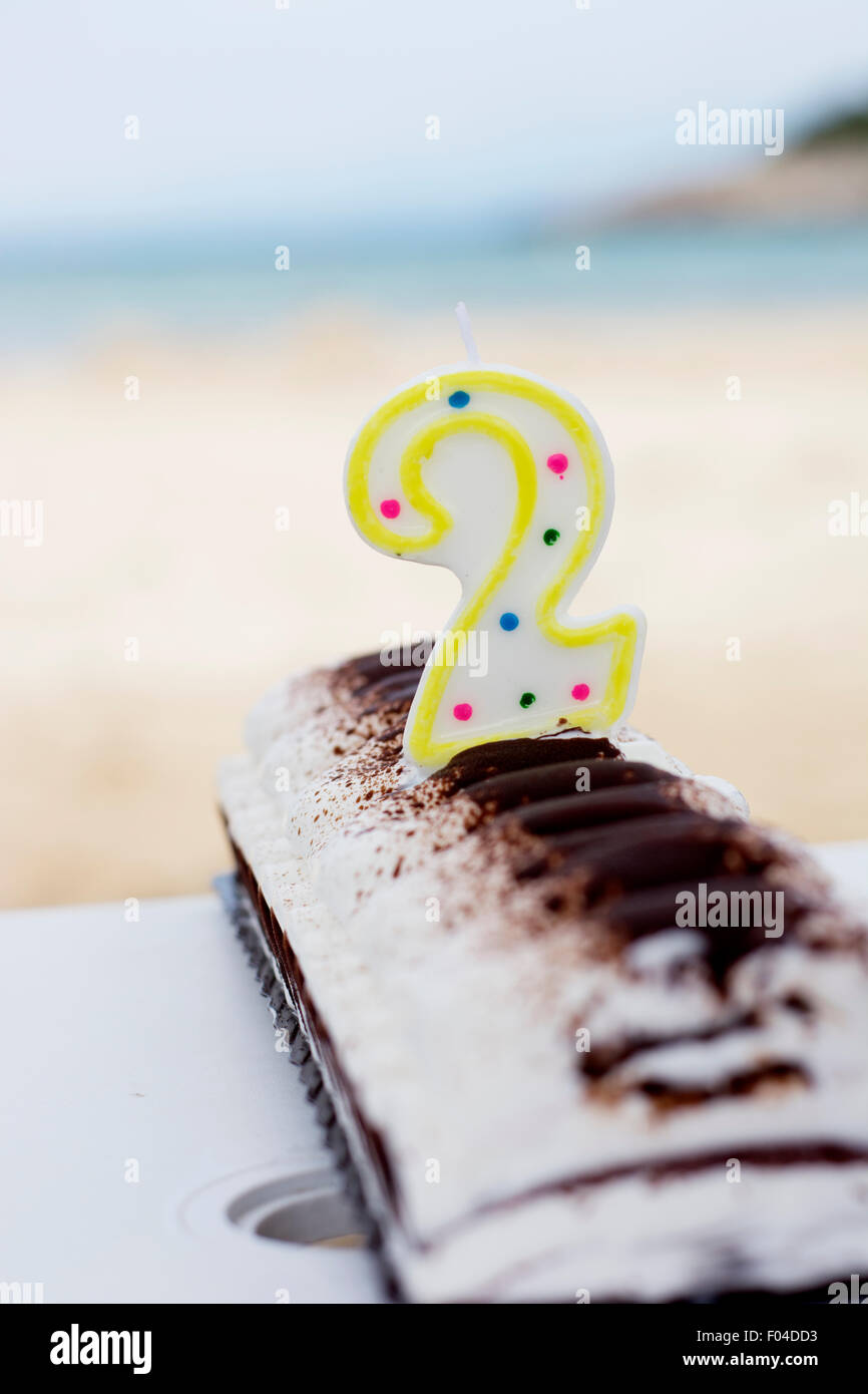 Ice cream birthday cake with candle number two on a beach Stock Photo