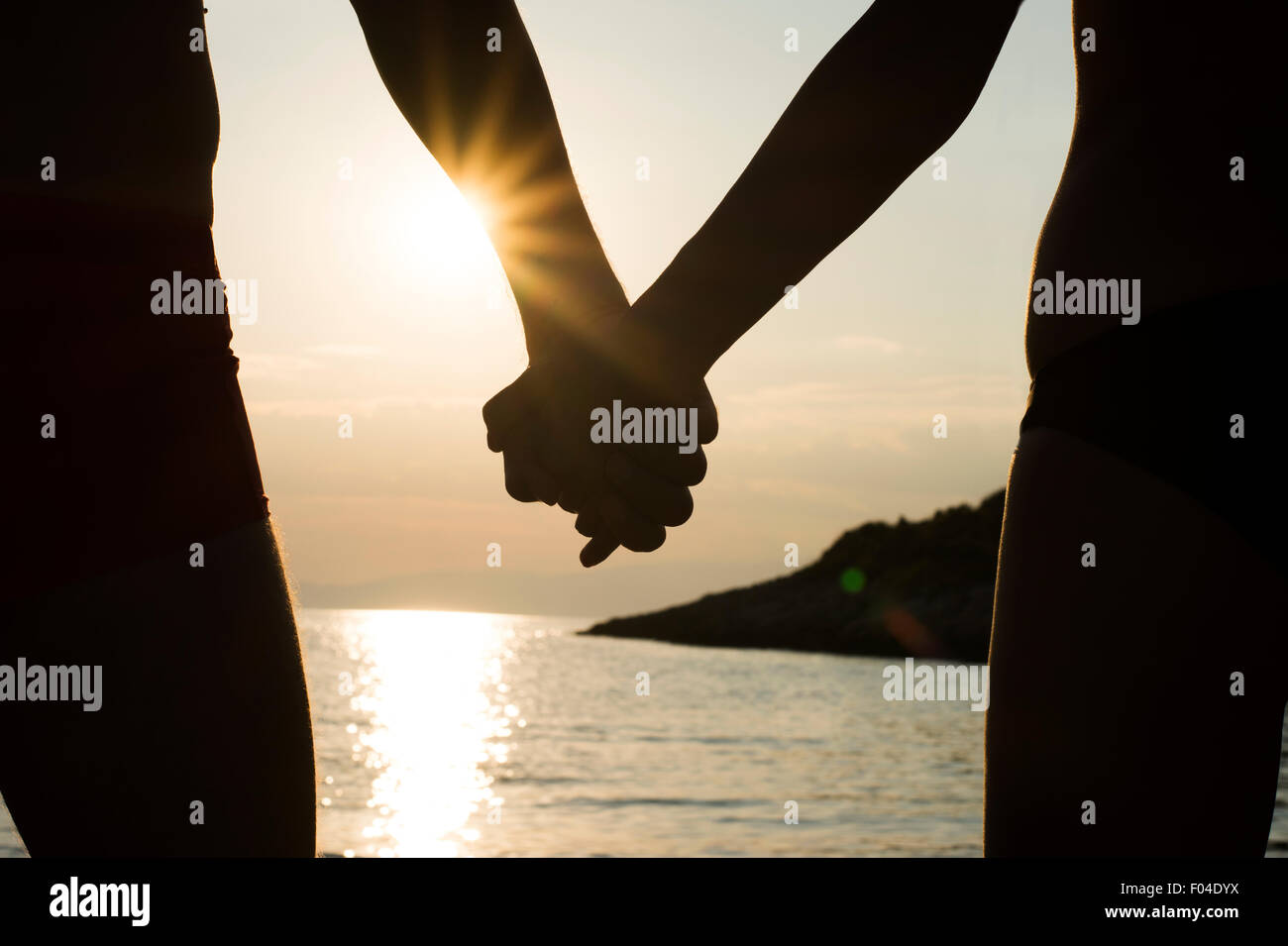 Closeup of a couple holding hands on a beach at sunset, silhouette effect. Stock Photo
