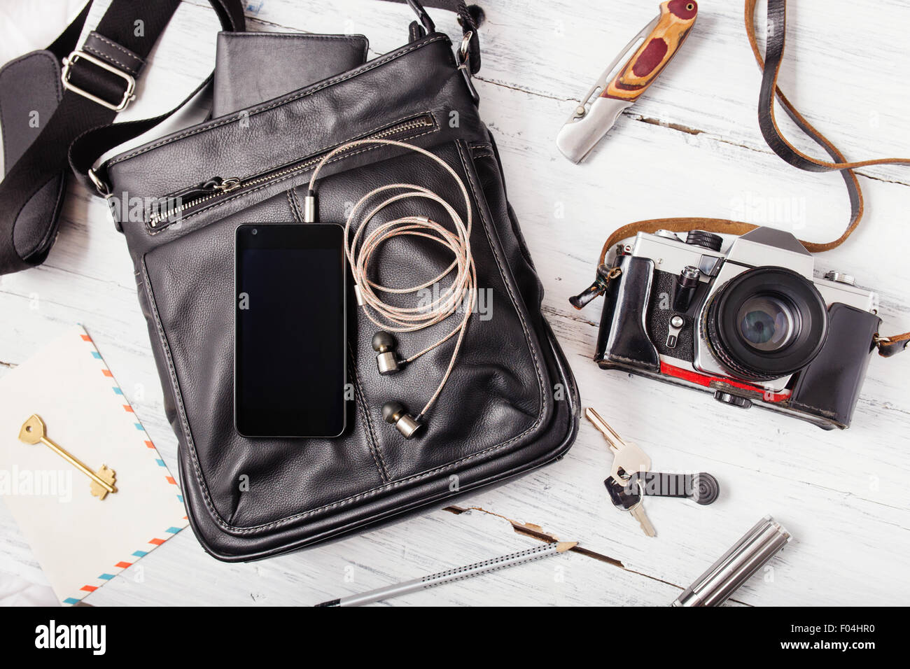 Objects on wooden background: leather bag, camera, smartphone, keys, knife. Outfit of young man. Stock Photo
