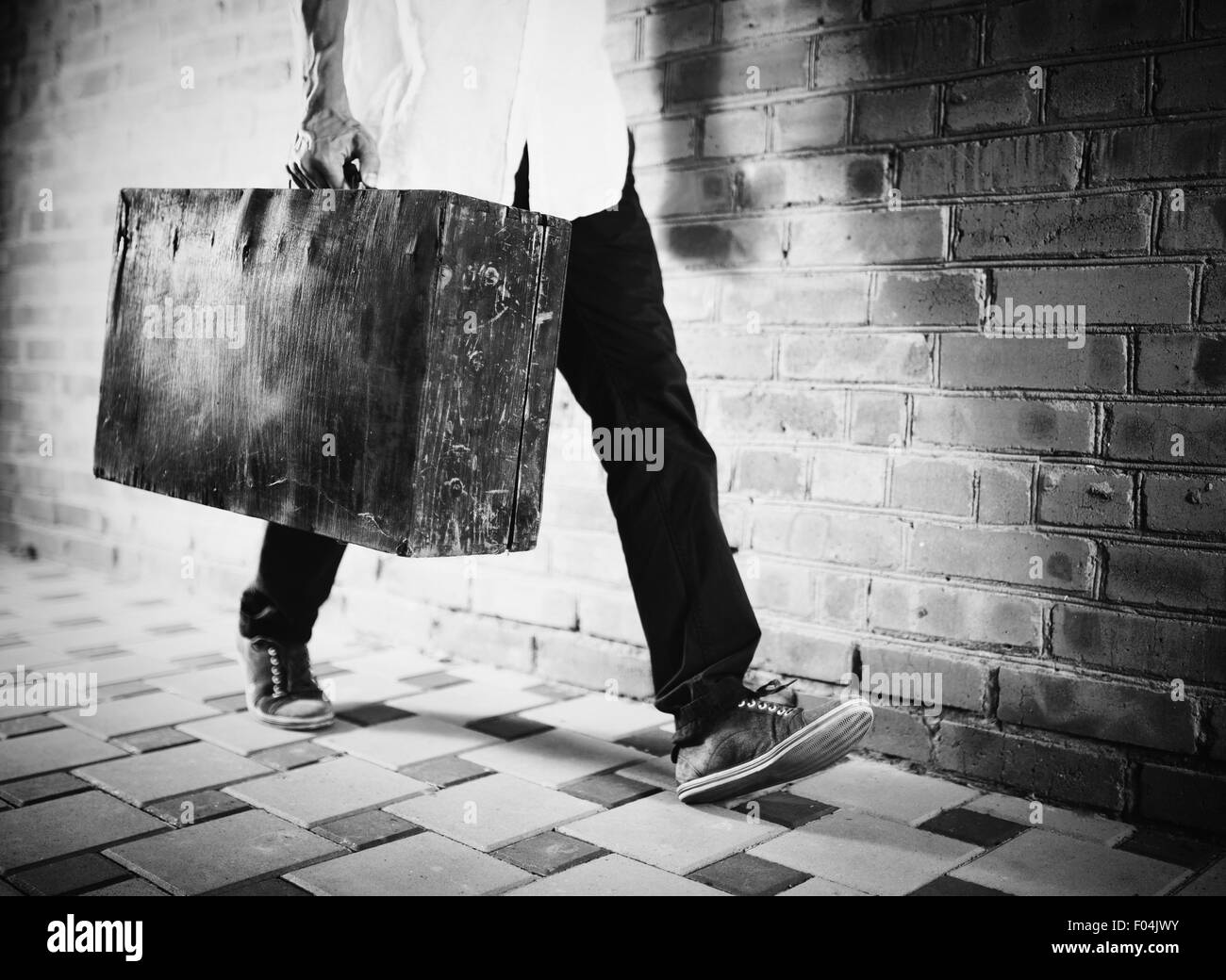 Young man walking along street with old suitcase, black and white photo Stock Photo