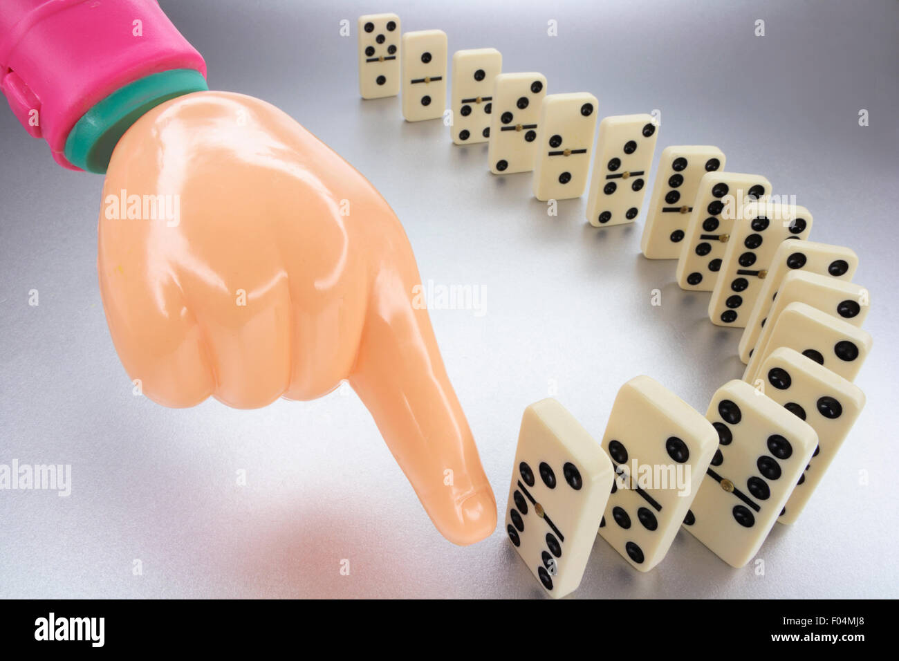 Plastic Hand and Row of Dominoes Stock Photo