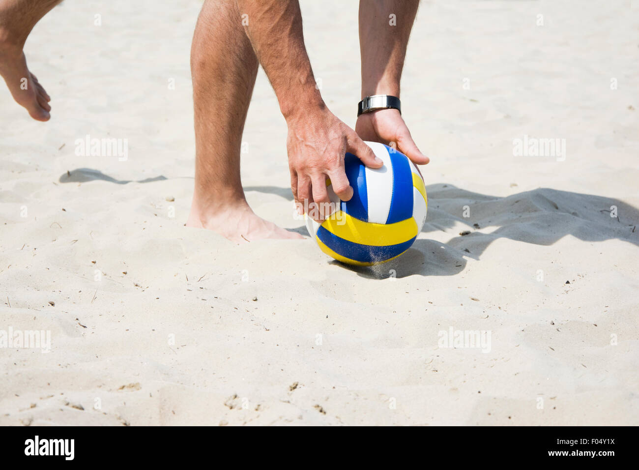 Male model picking up a beach volleyball from a sand. Volleyball is popular summer sports for both man and women. Stock Photo
