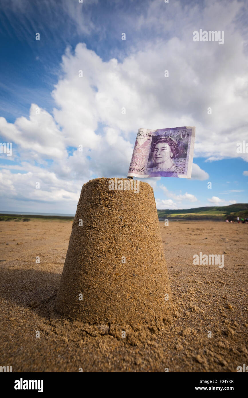 Concept photo of a sandcastle with a £20 note flag on a UK beach to illustrate the cost of School Holidays Stock Photo