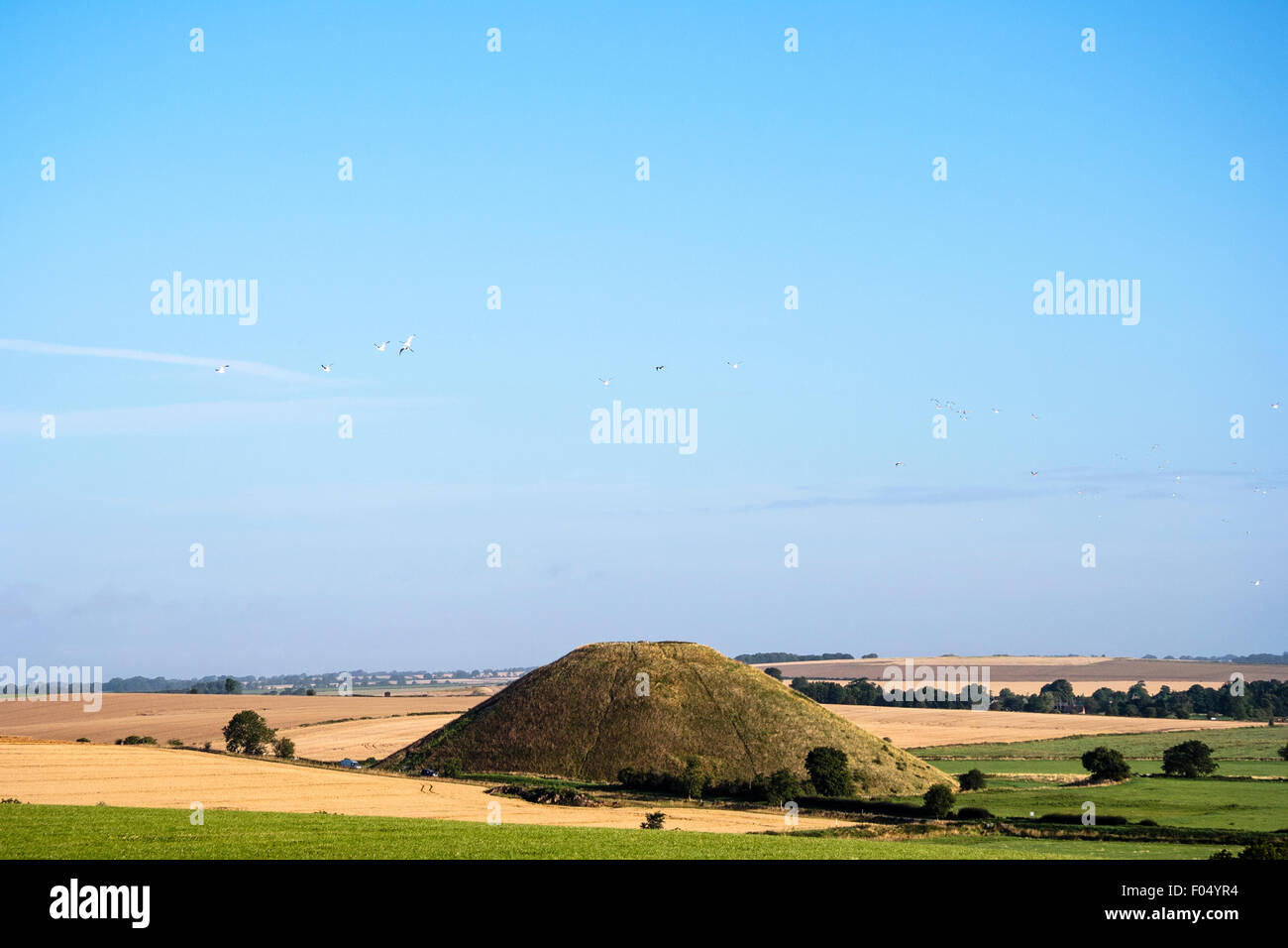Distant shot of Silbury Hill, man-made Neolithic mound in England. A 40 meter high man-made grass mound standing tall in the relatively flat landscape. Stock Photo