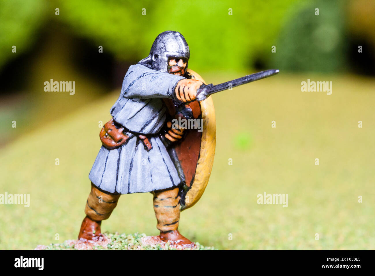 Close-up of metal painted model figure. King Arthur, in Saxon period costume, standing, thrusting a sword forward on table top battlefield. Stock Photo