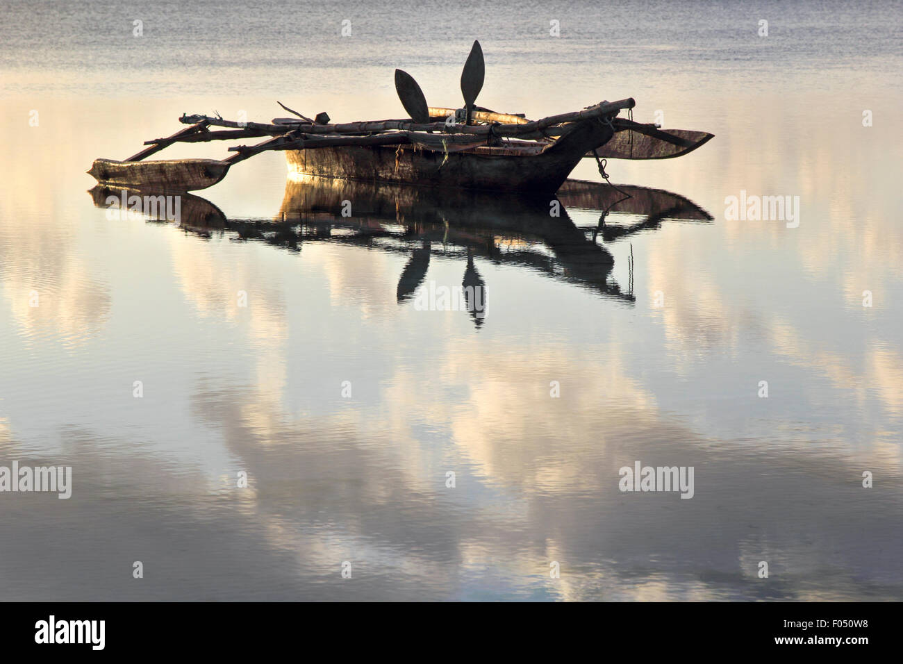 A dhow, traditional boat used in the Red Sea and Indian Ocean region, anchored on a very flat sea at dawn Stock Photo