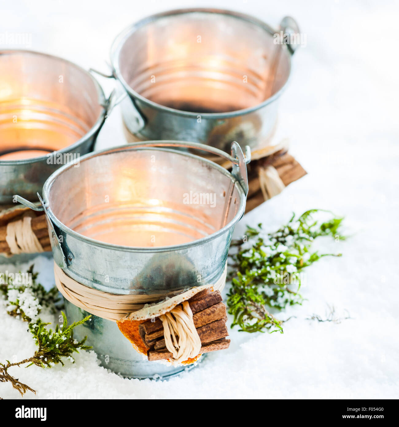three lit tealights in miniature zinc buckets decorated with raffia, dried orange peel and bundle of cinnamon bark Stock Photo