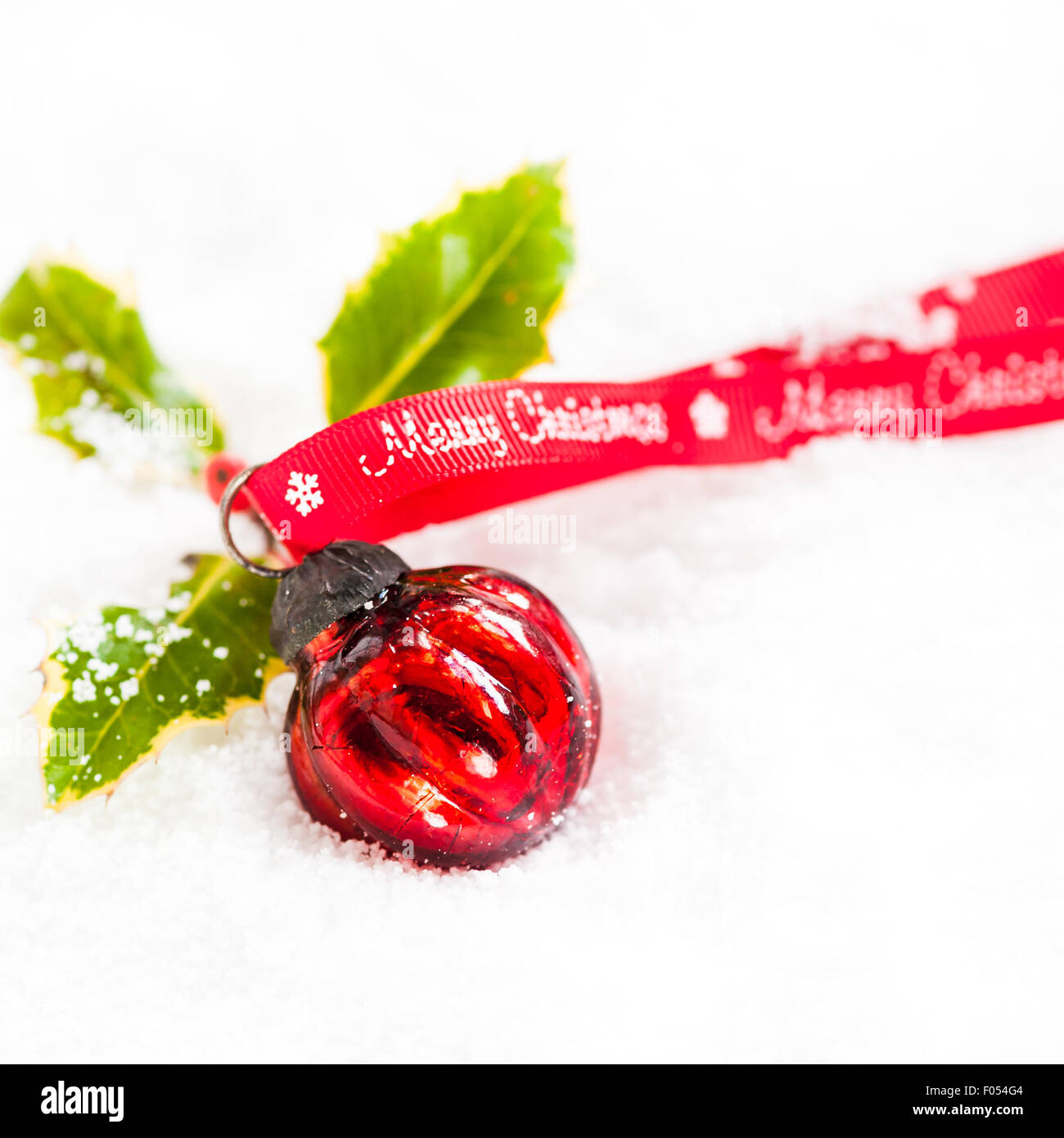 round red bauble with holly and Merry Christmas ribbon on snow Stock Photo