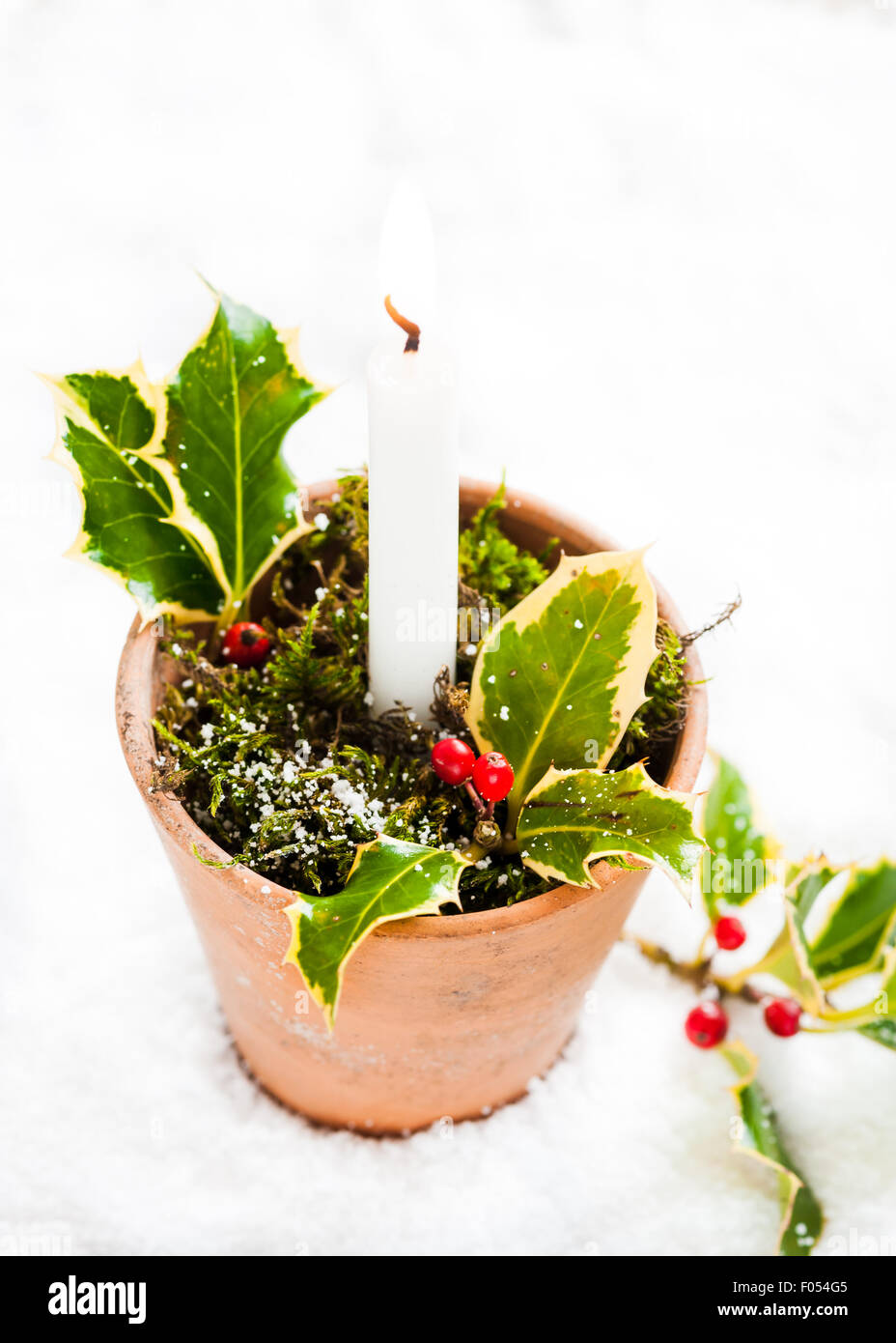 A candle holder made out of a vintage terracotta pot decorated with moss and a spring of holly Stock Photo