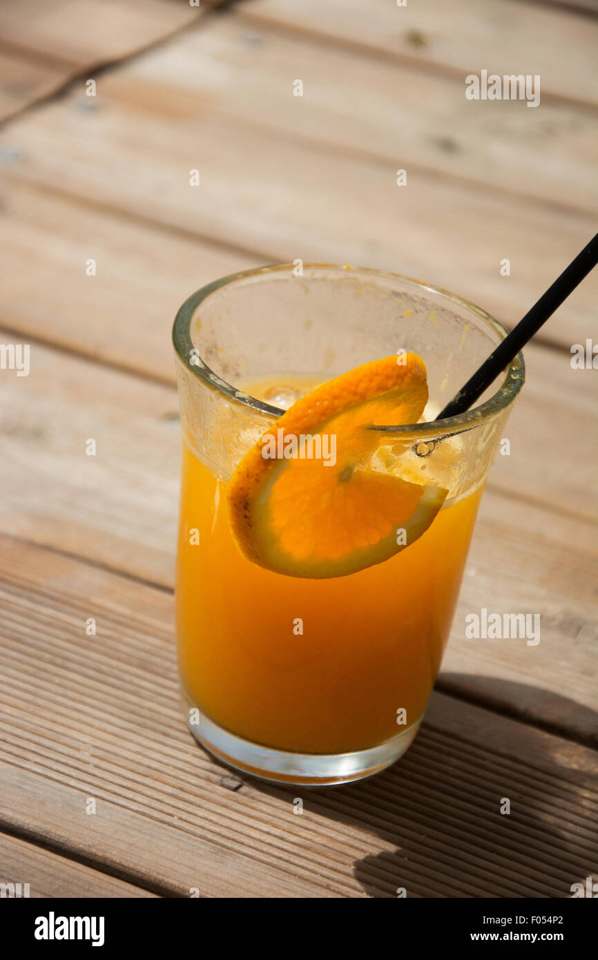 Glass full of fresh squeezed orange juice with ice cubes and black straw and piece of orange as a decoration. Stock Photo
