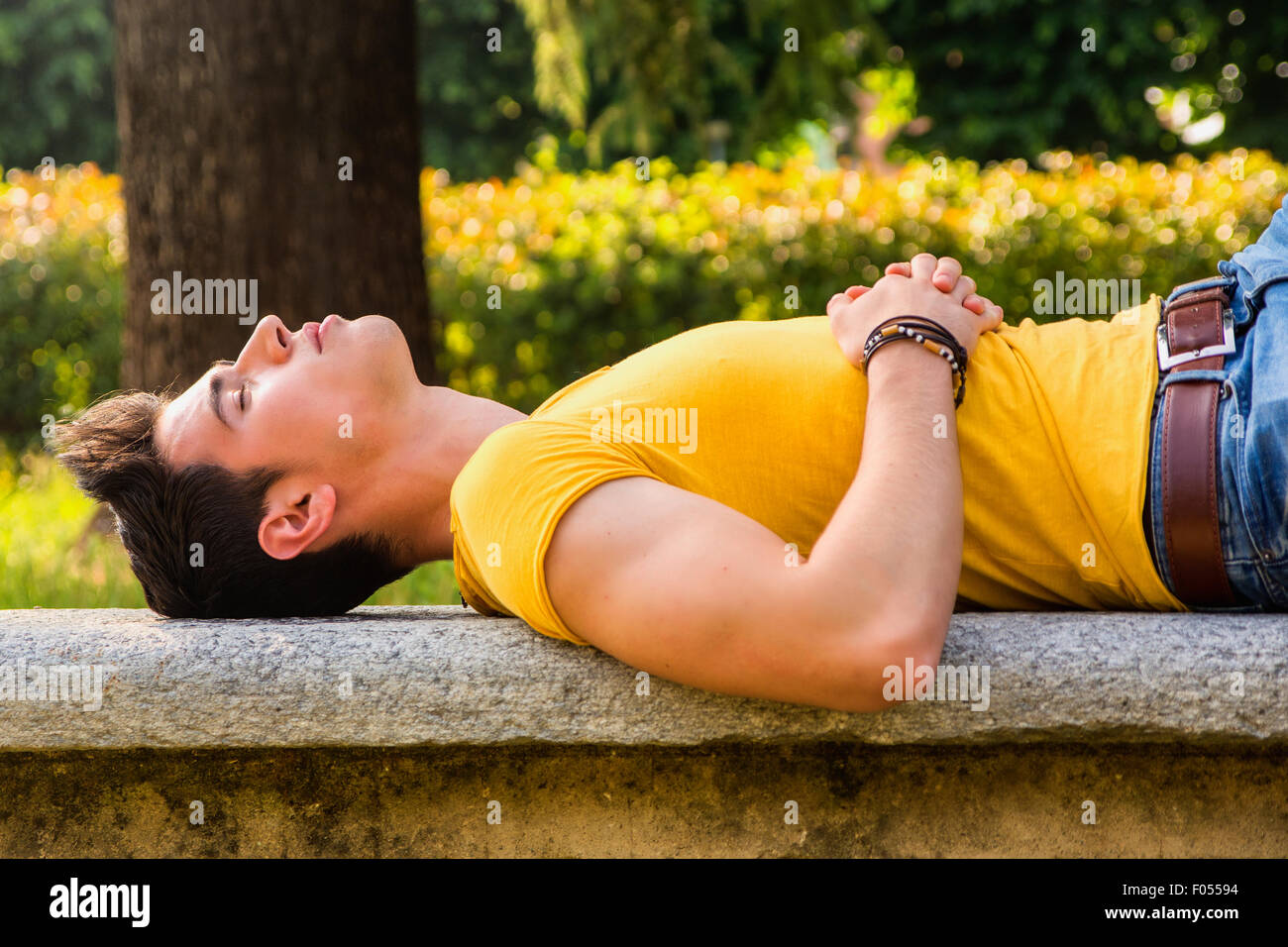 Attractive young man sleeping on stone bench outdoor in city park during day Stock Photo