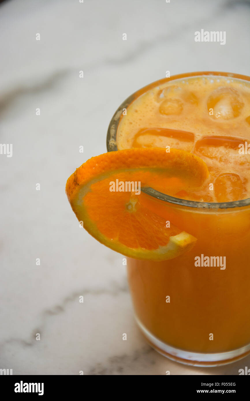 Closeup of a glass full of fresh squeezed orange juice with ice cubes and black straw and piece of orange as a decoration. Stock Photo