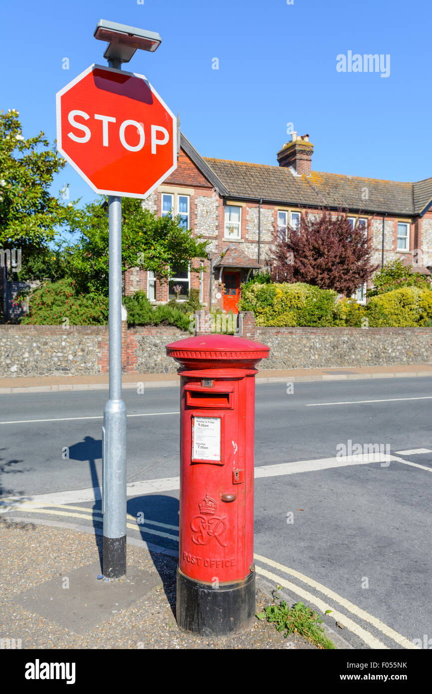 Red letter box. Royal Mail King George VI red Pillar Box on the corner of a road with a traffic stop sign in England, UK. Stock Photo