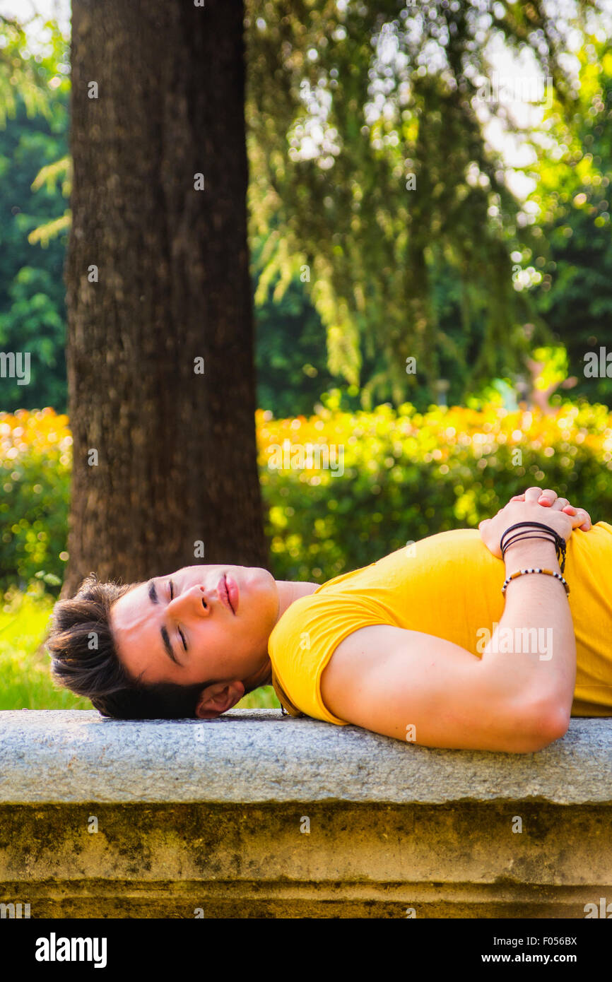 Attractive young man sleeping on stone bench outdoor in city park during day Stock Photo