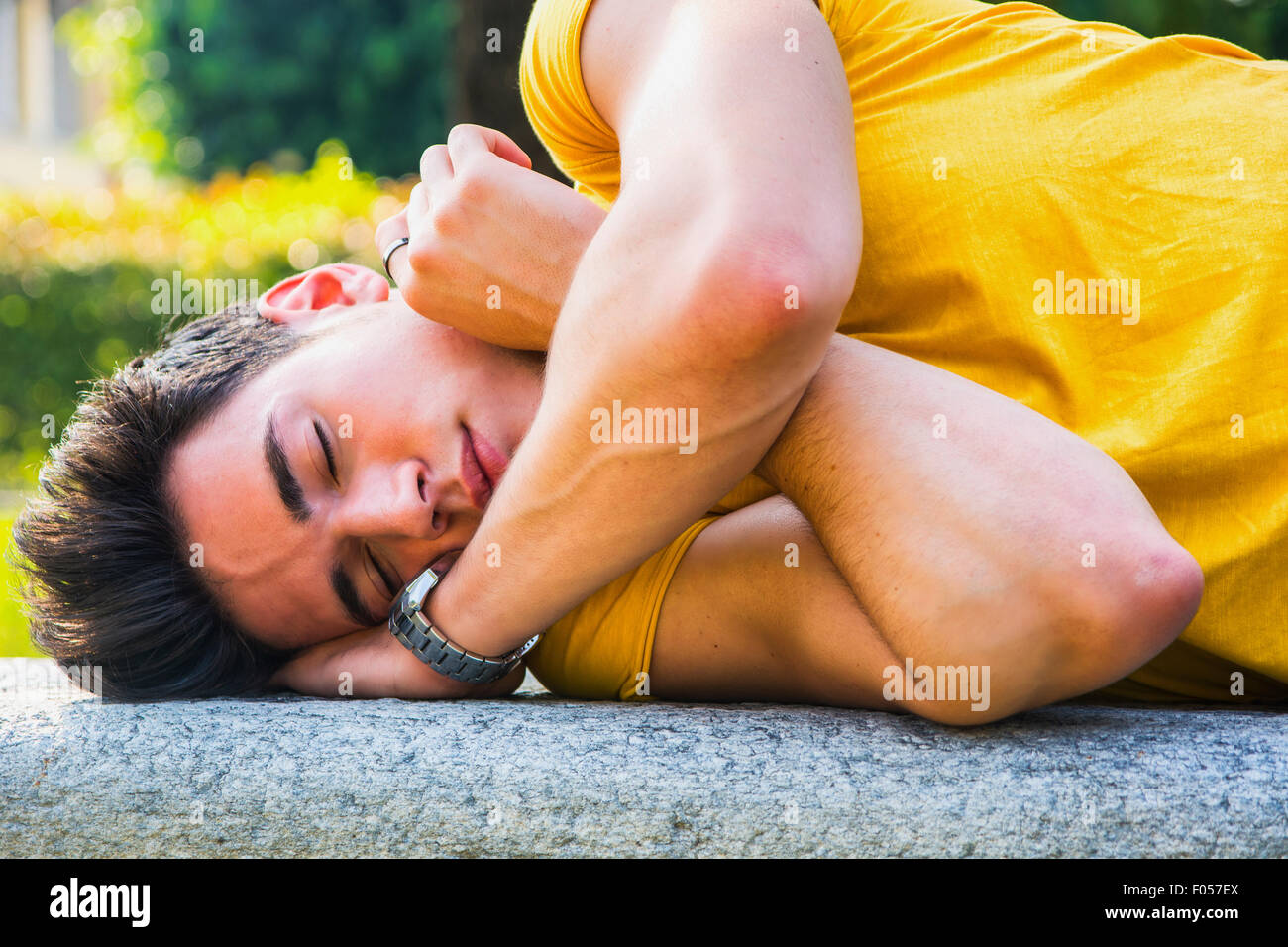 Attractive young man sleeping on stone bench outdoor in city park during day Stock Photo