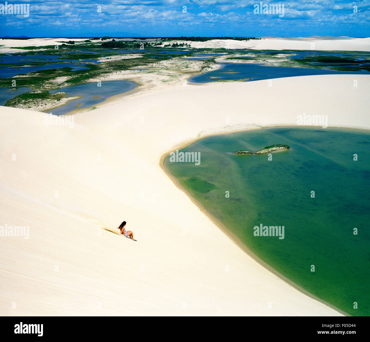 A woman rides a board down a sand dune at Dunas Tatajuba, just outside of Jericoacoara, Brazil. Stock Photo