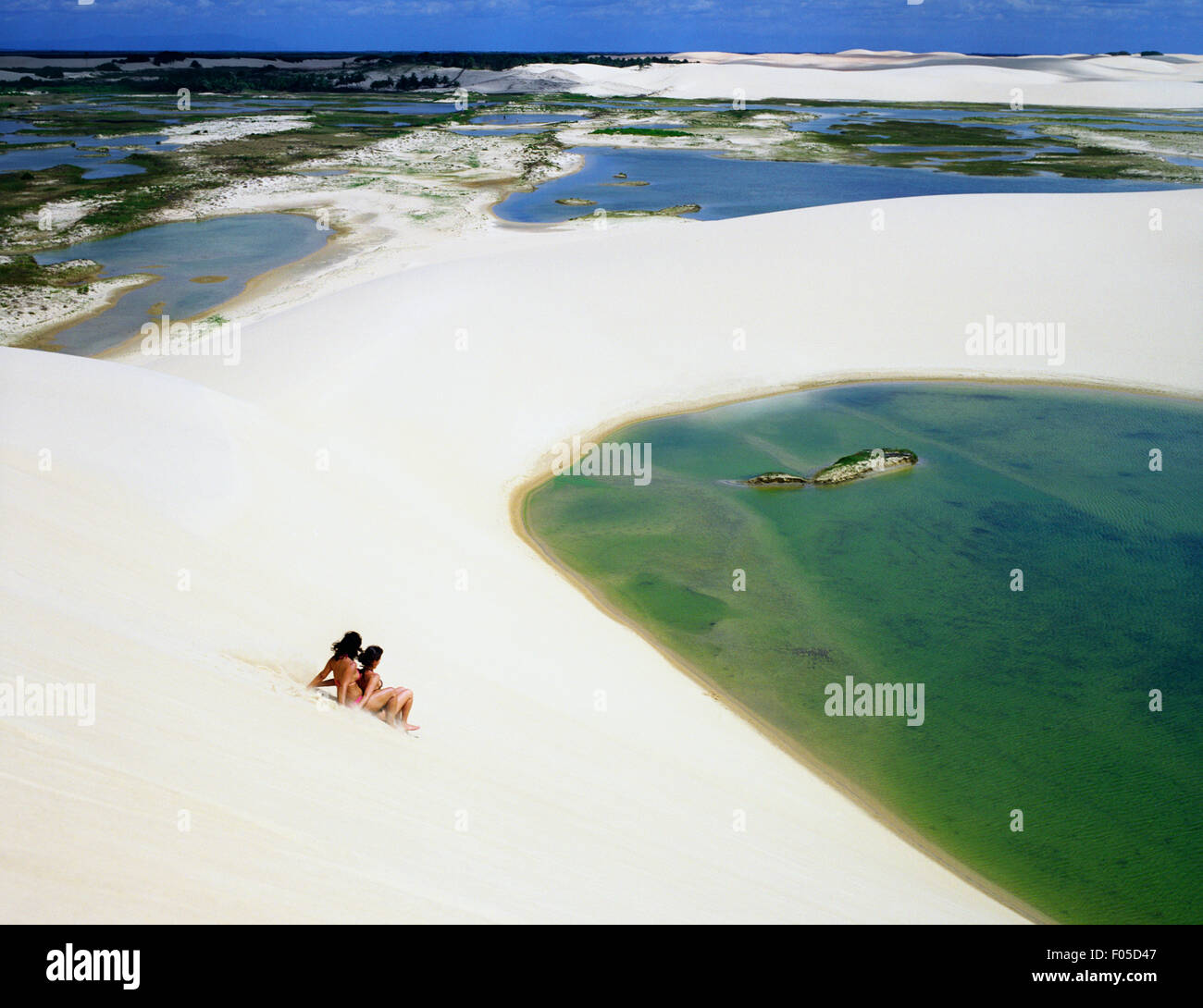 2 women friends ride a board down a sand dune at Dunas Tatajuba, just outside of Jericoacoara, Brazil. Stock Photo