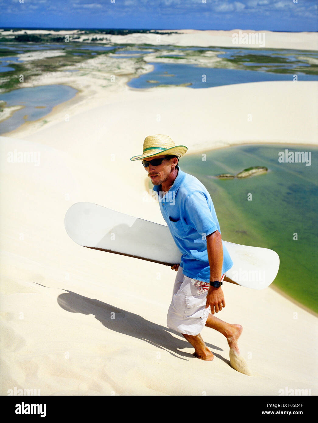 A Brazilian man climbs a dune to take another run sand boarding down a dune at Dunas Tatajuba, Jericoacoara, Brazil Stock Photo
