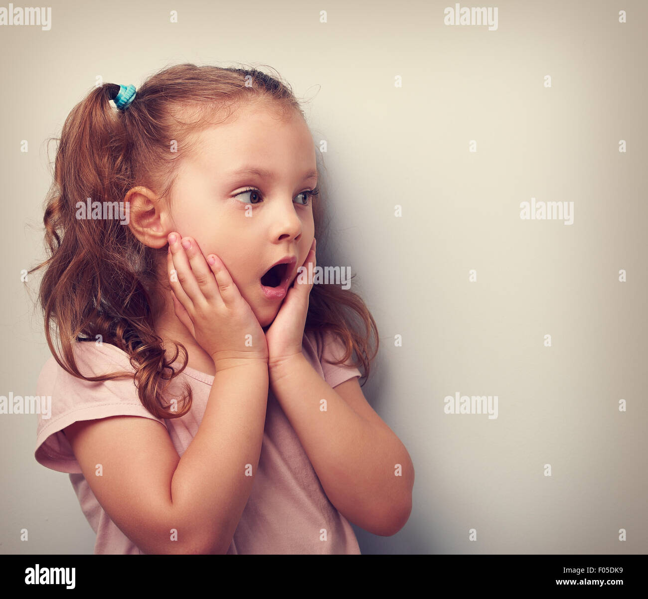Surprising kid girl with opened mouth and hand near face looking on. Toned portrait. Closeup Stock Photo