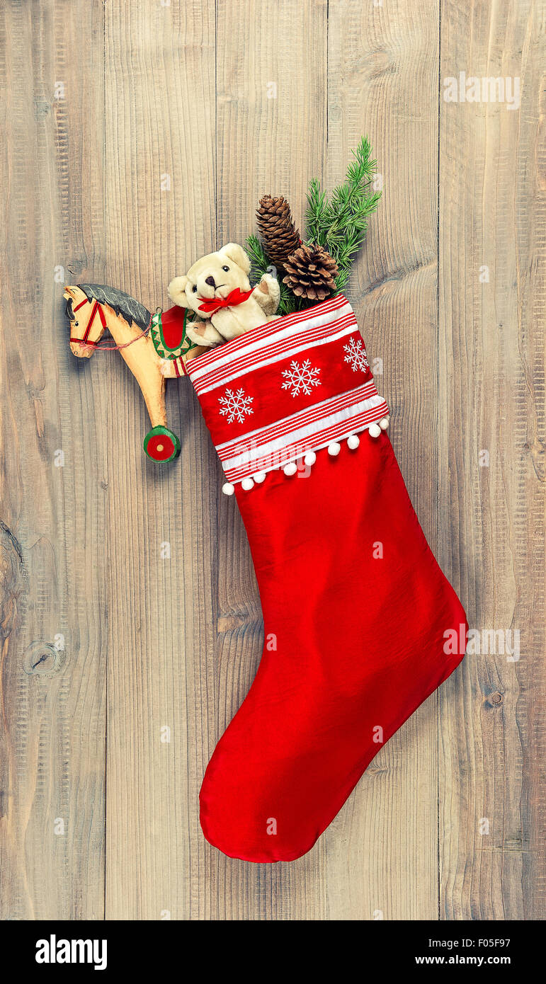 Christmas stocking with nostalgic vintage toys decoration and pine branch over wooden background. Retro style toned picture Stock Photo