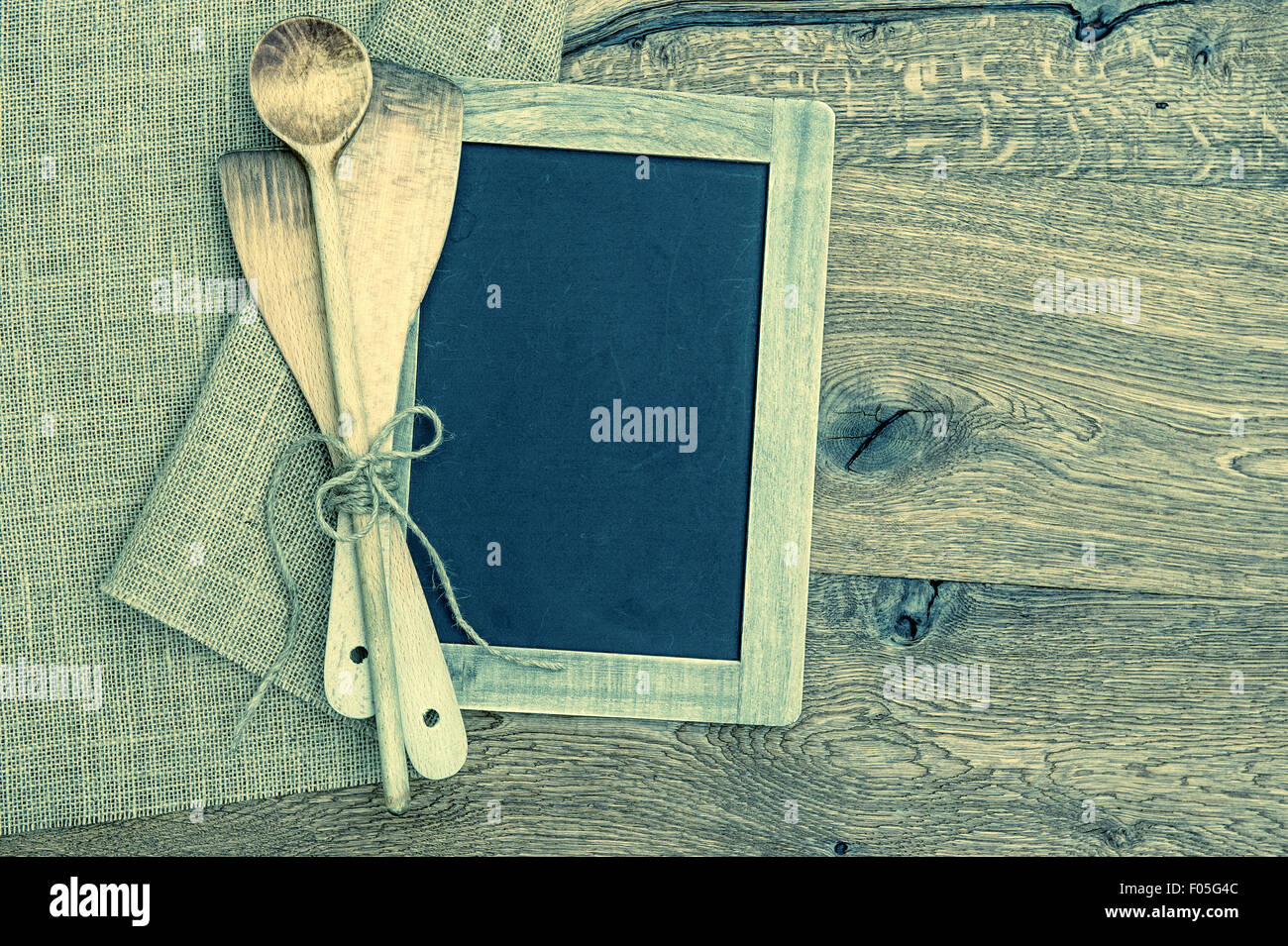 Old kitchen utensils and vintage blackboard on rustic wooden background. Retro style toned picture. Cross Processing Stock Photo