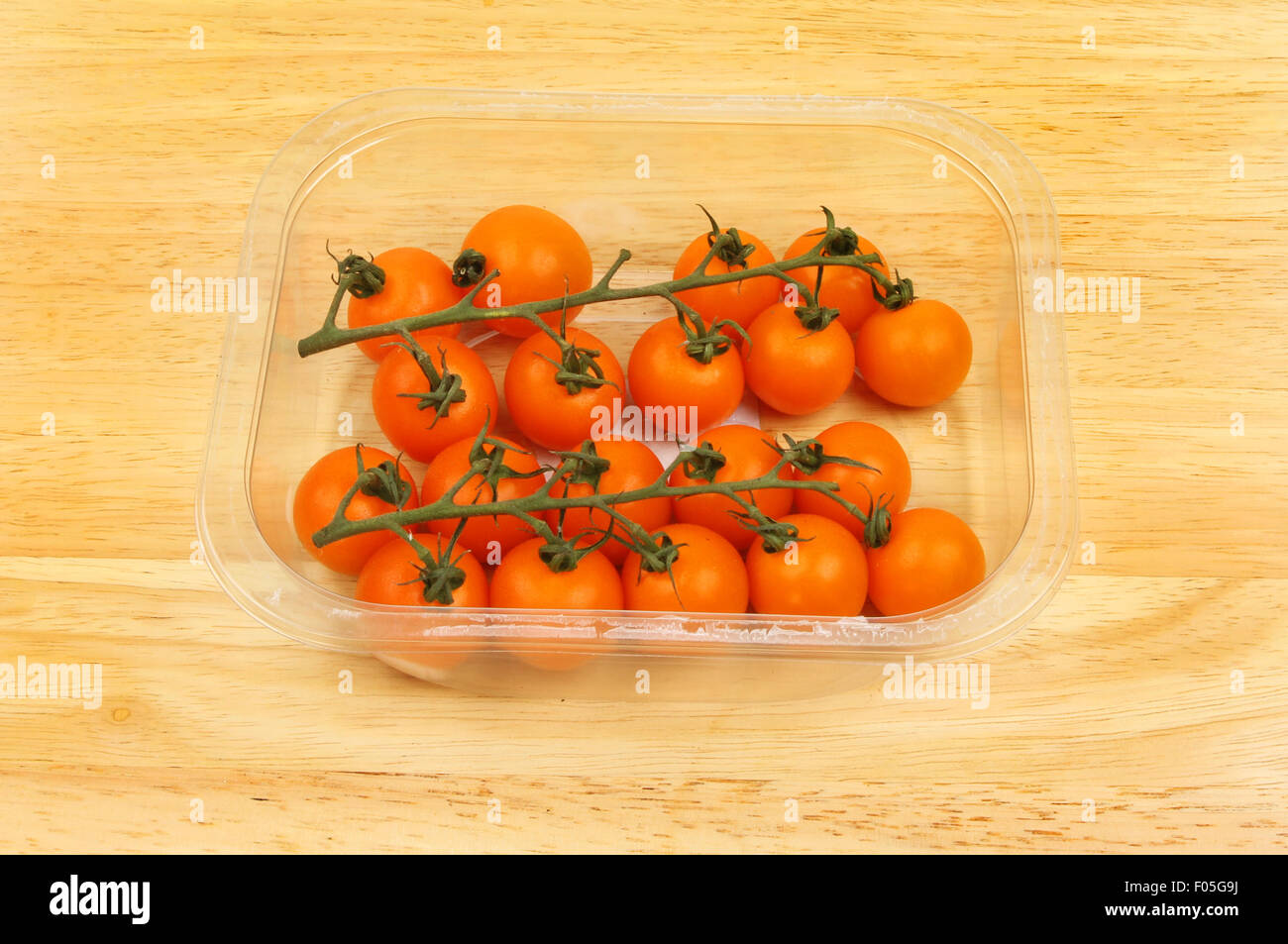 Golden vine tomatoes in a plastic carton on a wooden board Stock Photo