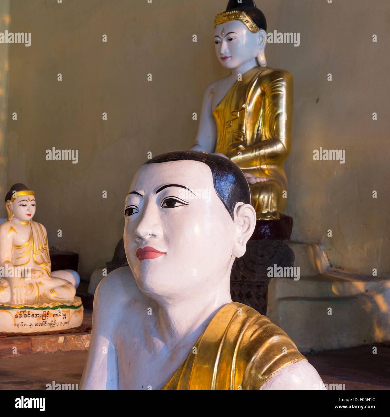 Buddha statues at Shwedagon Paya in Yangon, Myanmar. Foreground figure with atypical slanted shoulder pose and expressive face. Stock Photo