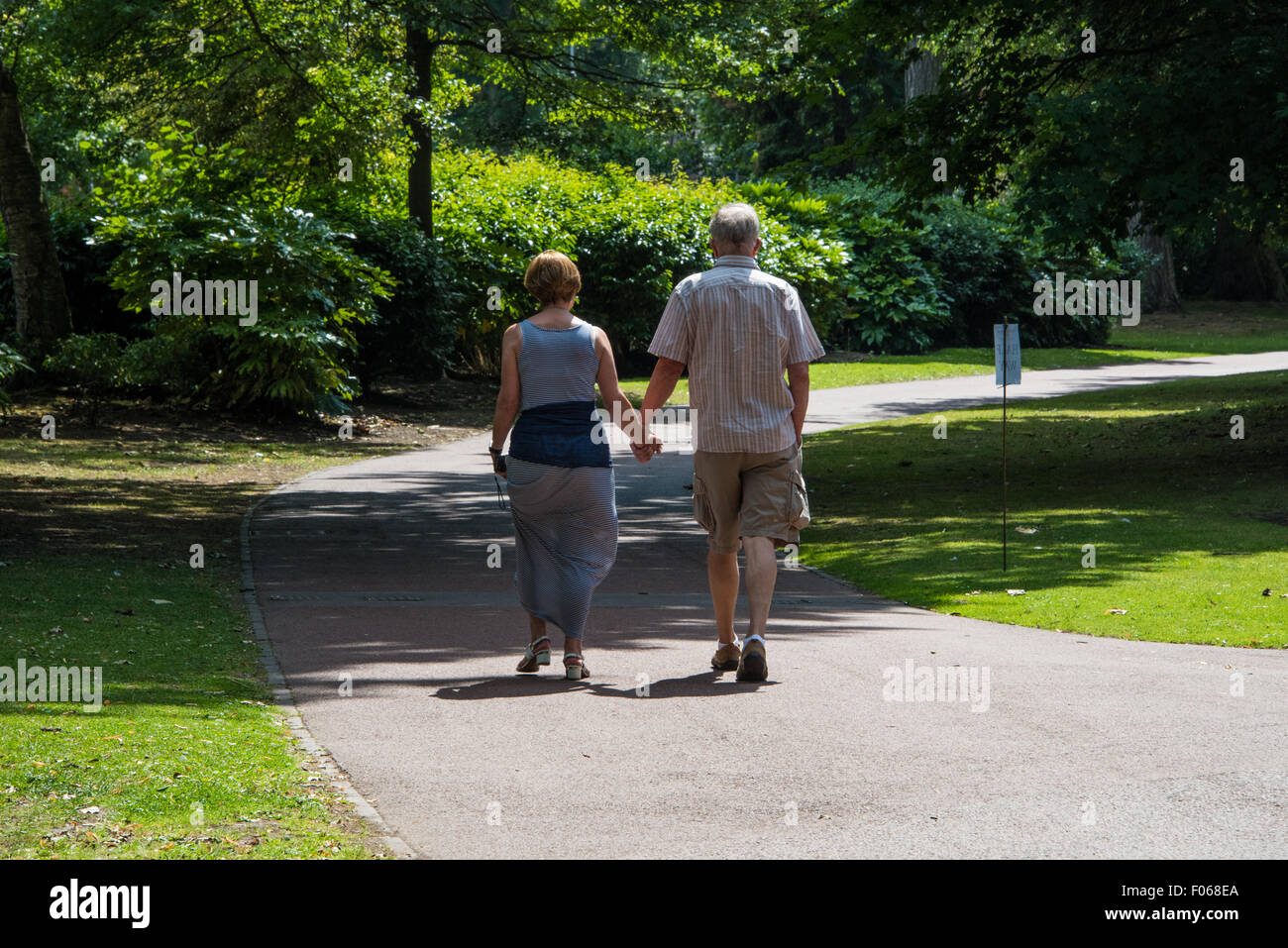 A senior couple holding hands walking through West Park on a summers day in Wolverhampton West Midlands UK Stock Photo