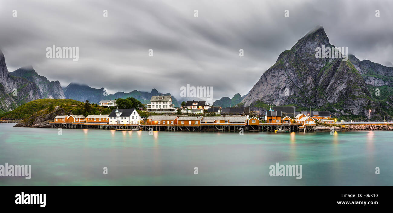 Panorama of  mount Olstind above the yellow cabins and turquise waters of Sakrisoy fishing village on Lofoten islands in Norway. Stock Photo