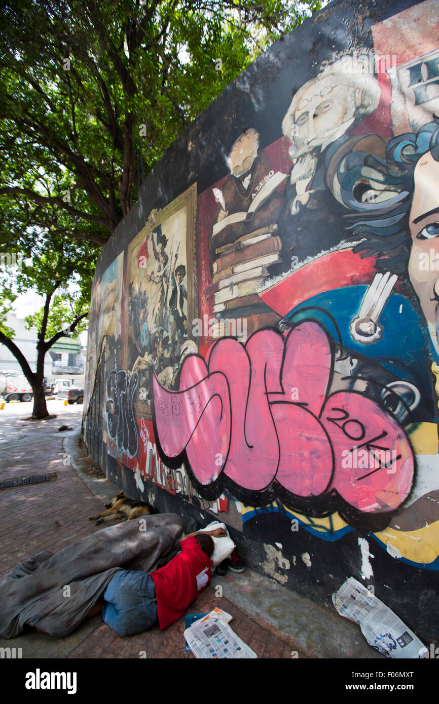 Unrecognizable poor man sleeping on the street of downtown Caracas with a graffiti of Simon Bolivar in the background. Stock Photo